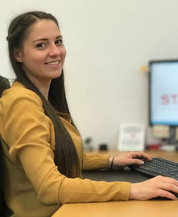 A portrait of a woman with brown hair sitting at a desk