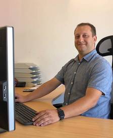 Portrait  of a man with short hair and a short sleeved shirt at a desk