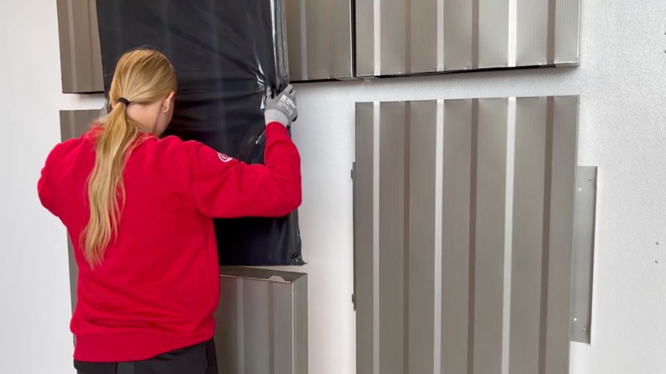 Person führt einen in schwarzen Plastik gepackten Dämmstoff in ein ESSONIC Gerät aus Metall ein.