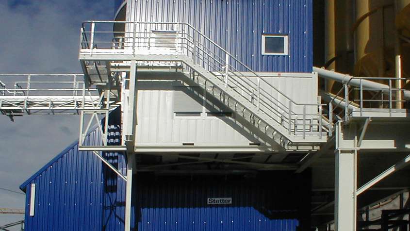 Cropped section of a building with a blue trapezodial sheet facade and a white, external staircase