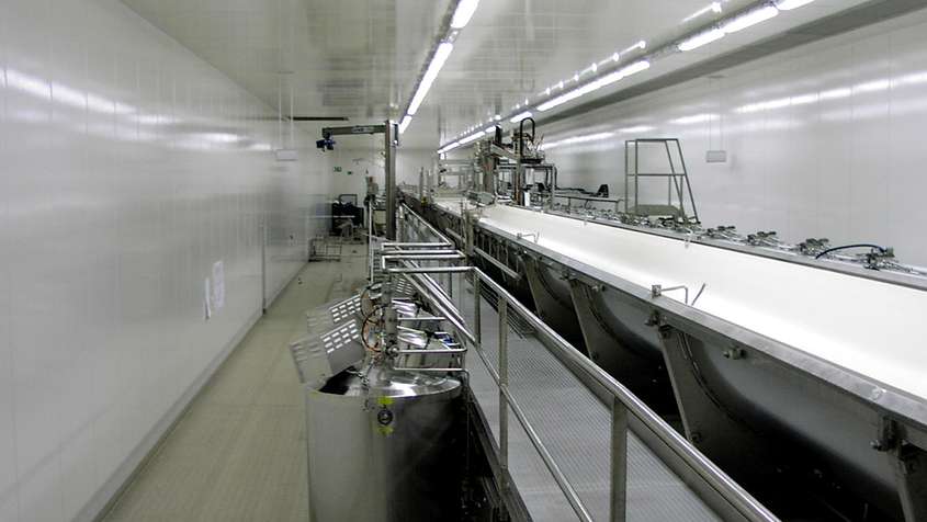 A sterile room full of technical equipment and a long, open-topped pipe with a stream of milk