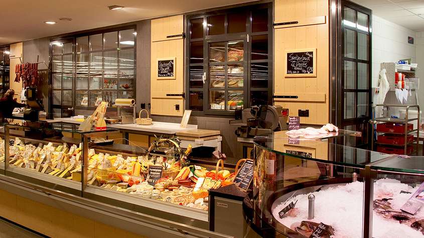 An elaborate cheese counter in front of a yellow wall with large display windows showing the cold storage room behind