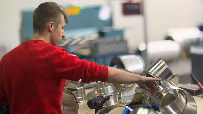 A young man putting together sheet metal pipes on a workbench