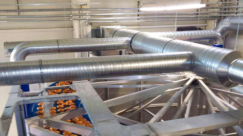 Pipes above a blue conveyor belt carrying breads