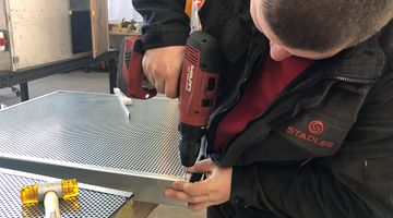 A man using a cordless screwdriver to fix a perforated metal plate to a frame