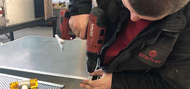 A man using a cordless screwdriver to fix a perforated metal plate to a frame