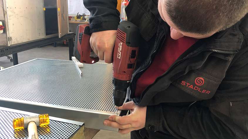 A man using a cordless screwdriver to fix a perforated metal plate to a frame