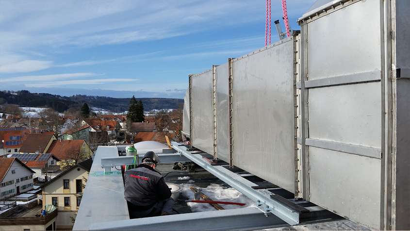 A mean wearing a helmet working next to a large metal construction on the roof of a high building