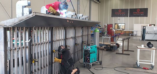 Two men working on a large metal construct in a workshop