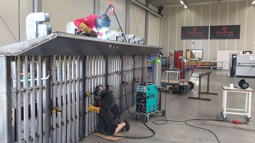 Two men working on a large metal construct in a workshop