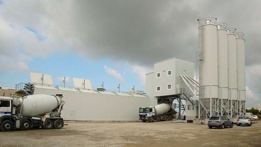 Lightgrey building with transit truck mixers below a grey sky