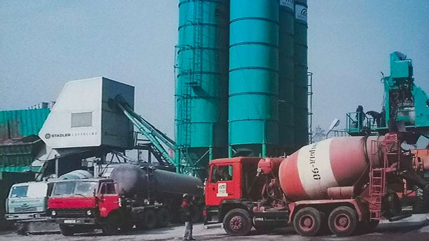 Red transit mixing trucks in front of a teal coloured silo complex