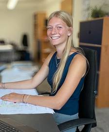 A young woman sitting at an office desk, smiling at the camera