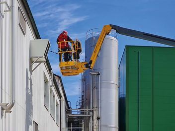 Schallmessung von zwei Menschen in einem Hebekrahn an einer Industriefassade