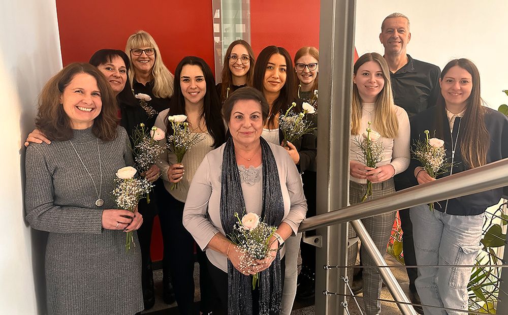 Eine Frauengruppe mit Blumen in der Hand, die in einem Treppenaufgang stehen. Seitlich rechts ein Mann.