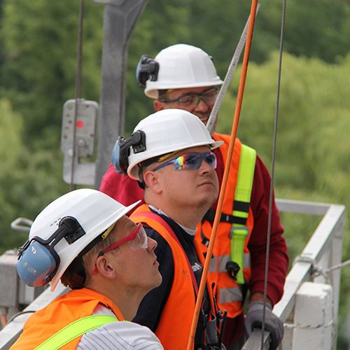 Three men with construction worker helmets staring curiously at something outside the frame