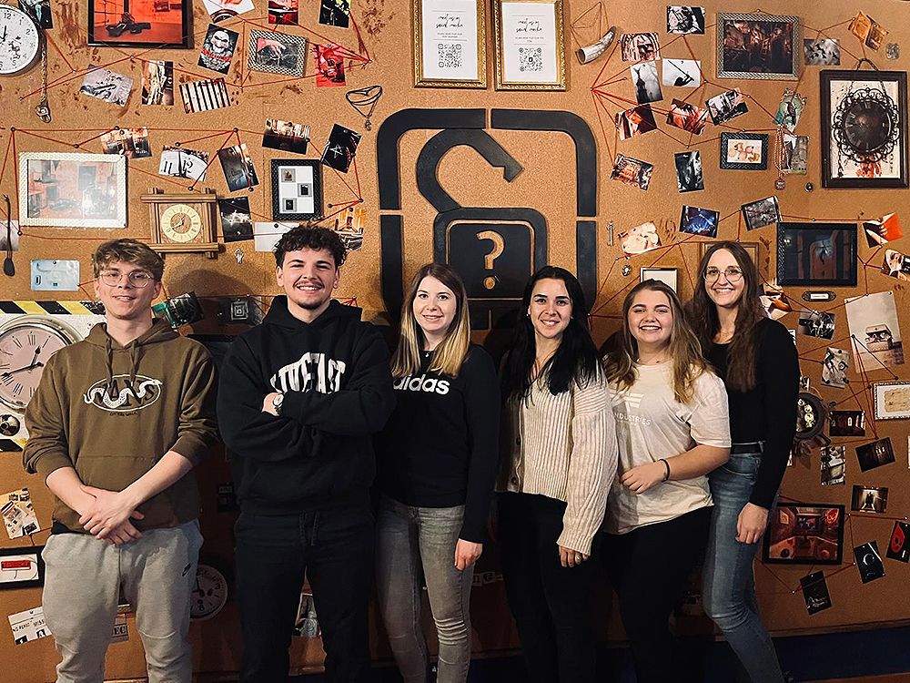  A group of six people standing in front of a puzzle wall