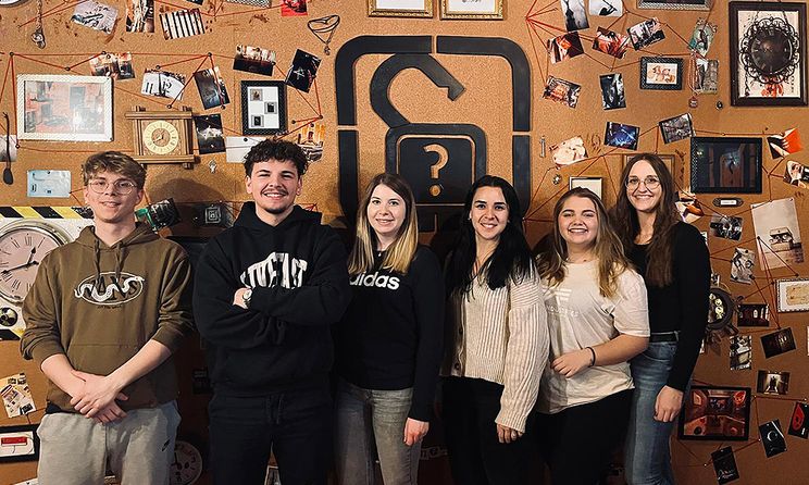  A group of six people standing in front of a puzzle wall